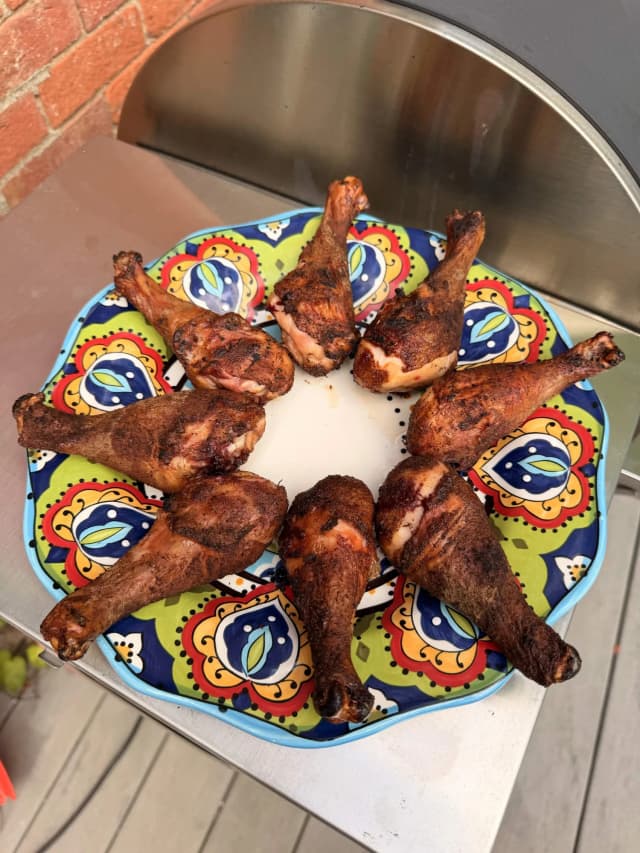 Cooked chicken drumsticks arranged on a colorful decorative plate next to a metal bowl
